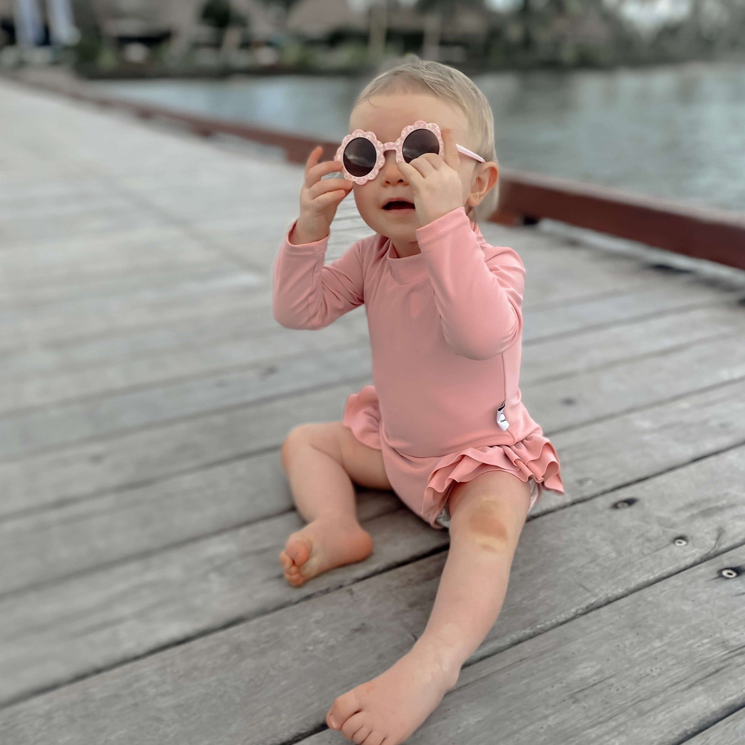 Baby girl wearing sunglasses and a pink long sleeve swimsuit