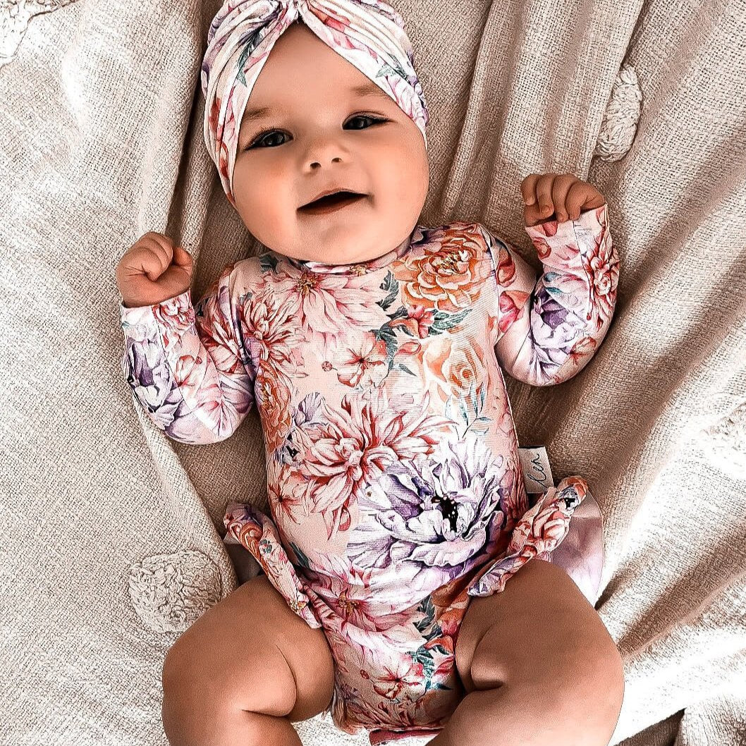 Cute baby girl wearing a floral nappy change infant swimsuit that has snaps for easy access to nappy changes. The baby girl is wearing a matching swim turban.