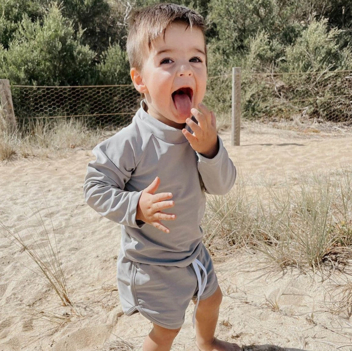 toddler on the beach playing in a grey two piece swim set with large rear zip