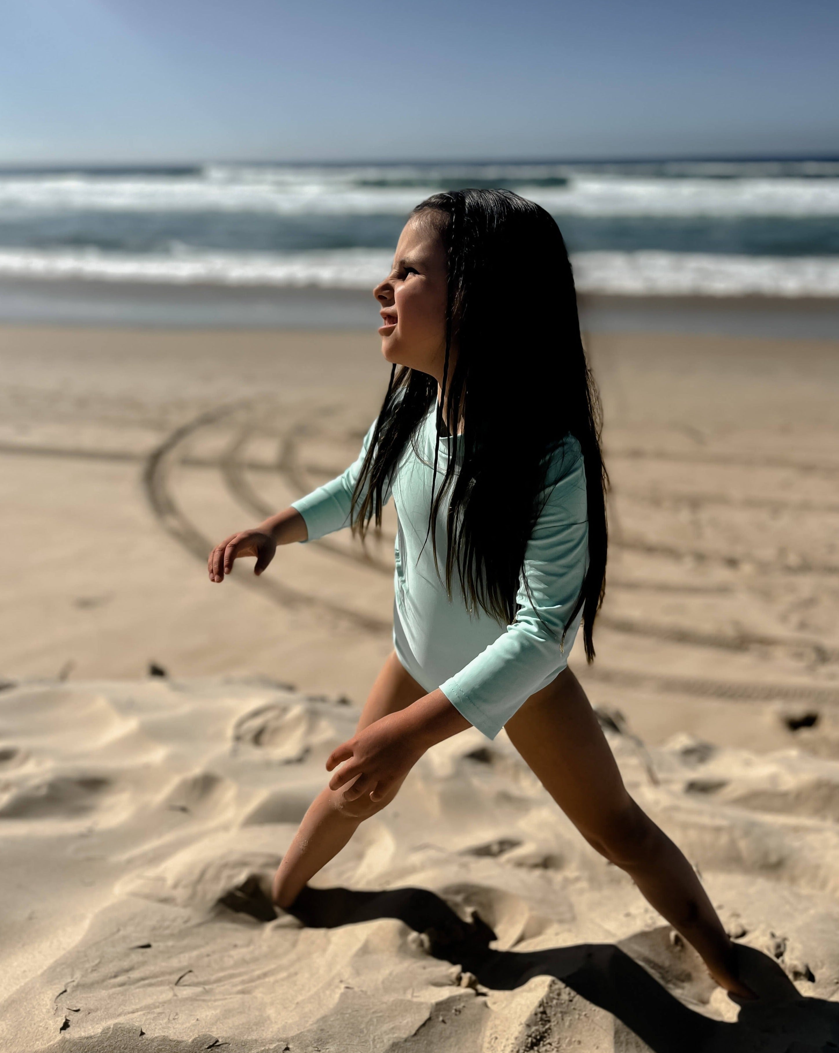 young girl at beach in a bright green swimsuit with nappy change snaps