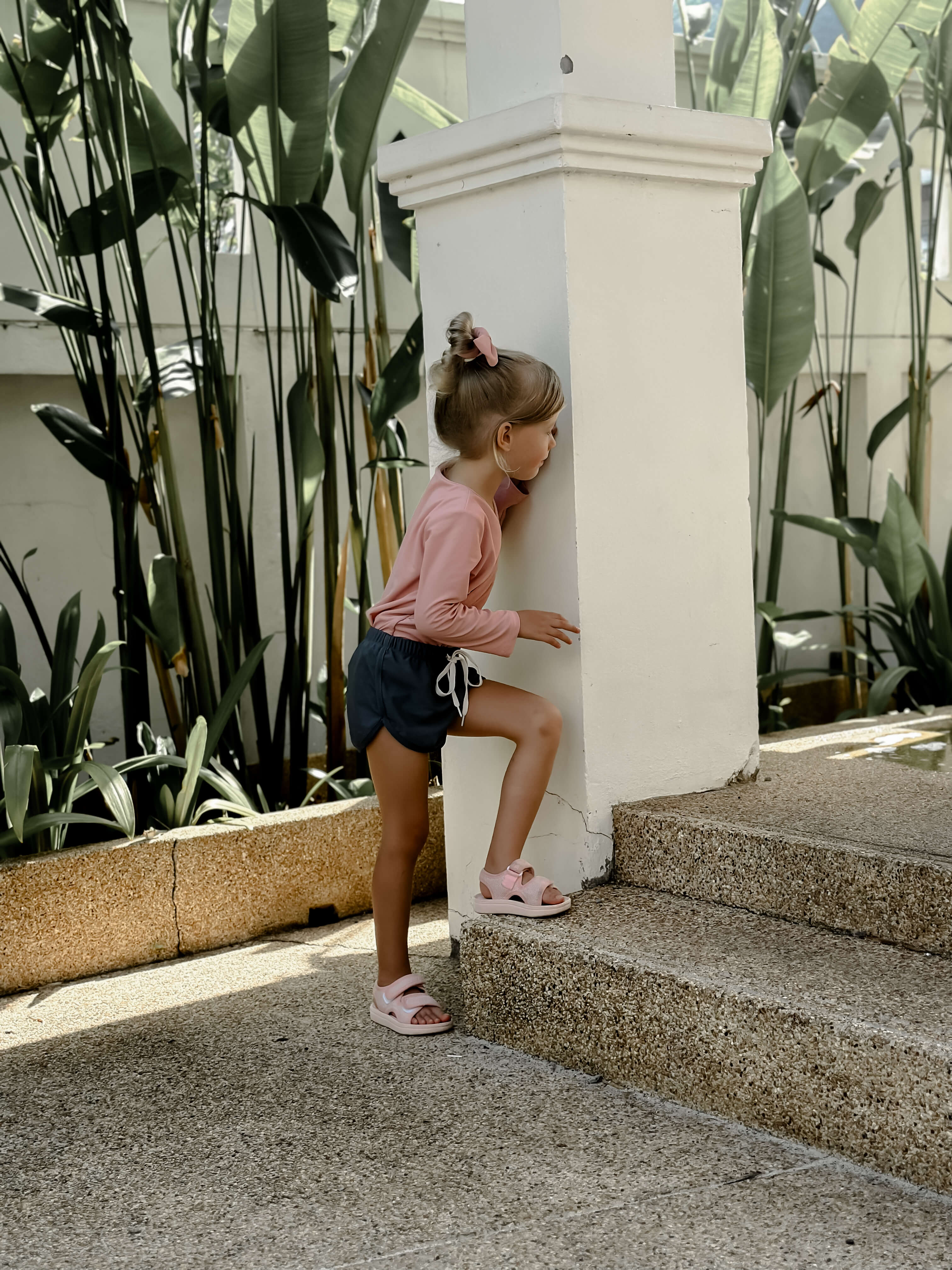 young girl wearing a pink rash guard swim top and navy swim shorts