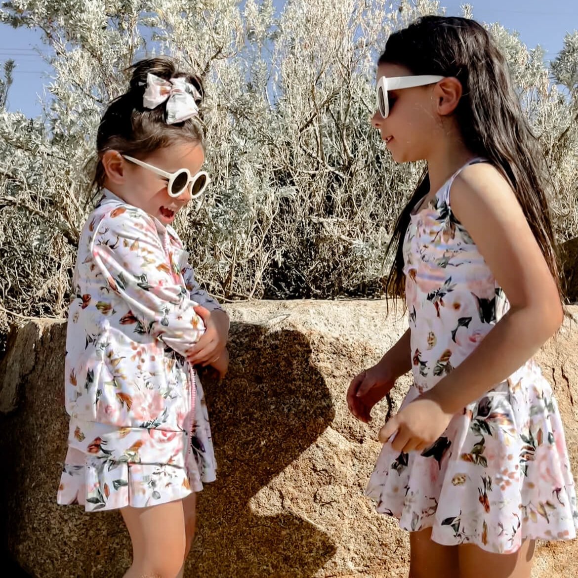 two girls wearing matching swim dresses with nappy change snaps, and long sleeve jackts