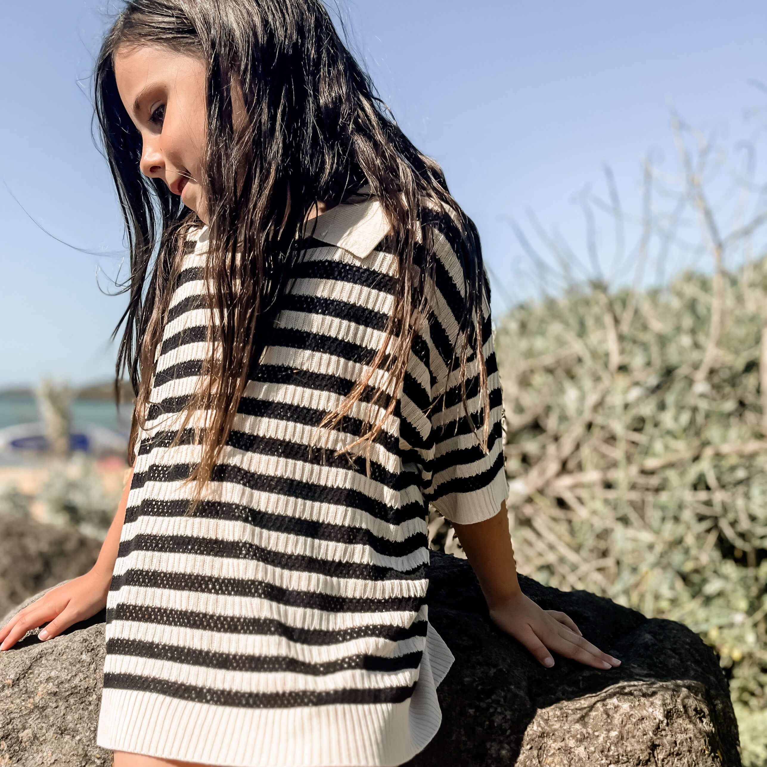 Young girl at the beach wearing a unisex children's black and white striped knit with a collar